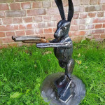 Metal sculpture of hare with gun on walled background