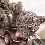 Large metal horseshoe sphere sculpture being unloaded from truck