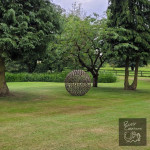 Sphere sculpture sitting in landscaped ground with trees