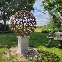 Metal sphere sculpture on plinth within large garden