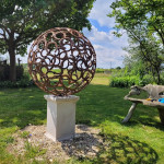 Metal sphere sculpture on plinth within large garden