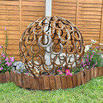 Metal sphere sculpture nestled in garden flower boarder